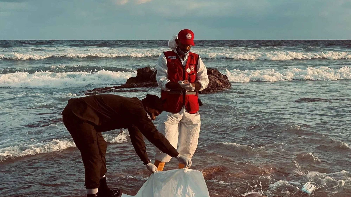 অভিবাসীবাহী নৌকা ডুবে যাওয়ার পর সুরমান শহরের উপকূলে একটি লাশ রাখার ব্যাগের পাশে দাঁড়িয়ে আছেন রেড ক্রিসেন্টের একজন সদস্য।  ছবি- সংগৃহীত